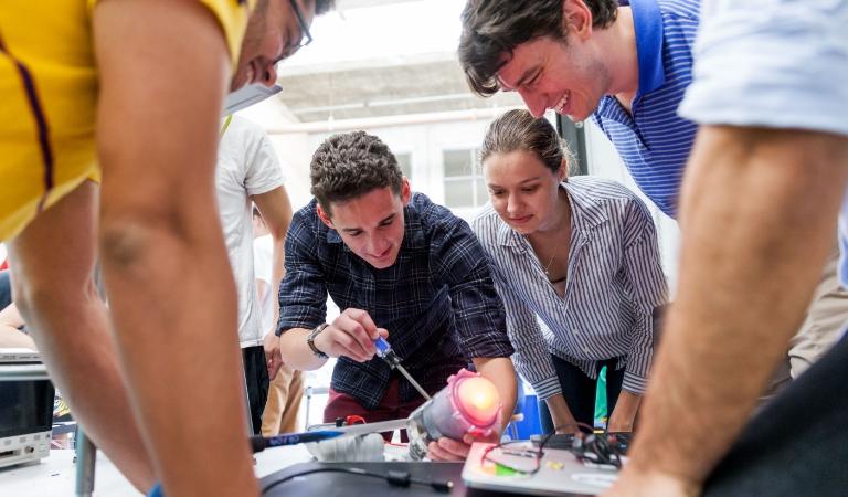 Students watch as another adjusts a light on a device.